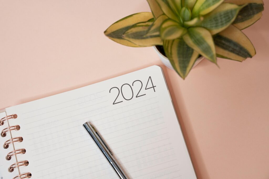 A simple 2024 planner with a pen on a peach background beside a potted plant, perfect for organization and planning.